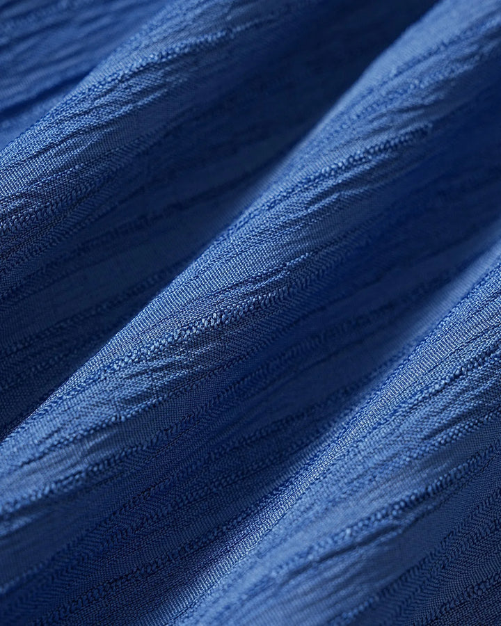 Model in a blue pleated midi dress styled in a lifestyle setting
