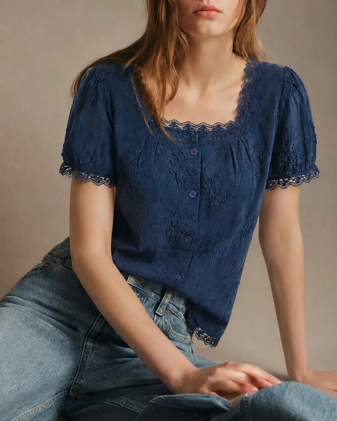 Model wearing a blue embroidered blouse with lace trim, facing forward