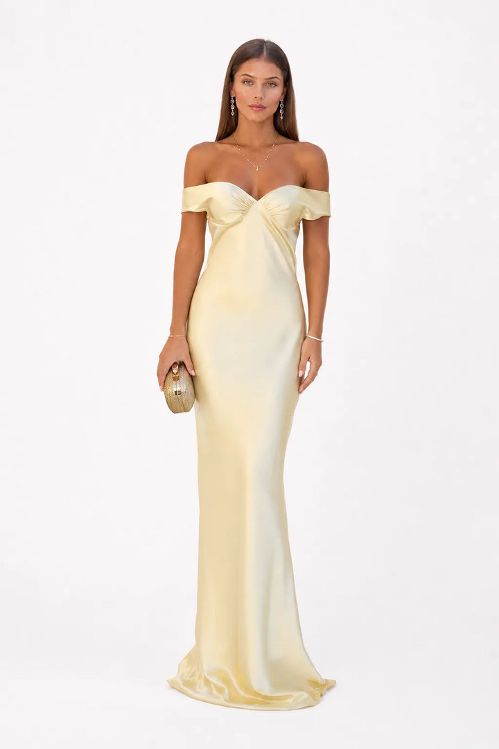 Woman in a yellow off-shoulder satin gown standing in a contrapposto pose