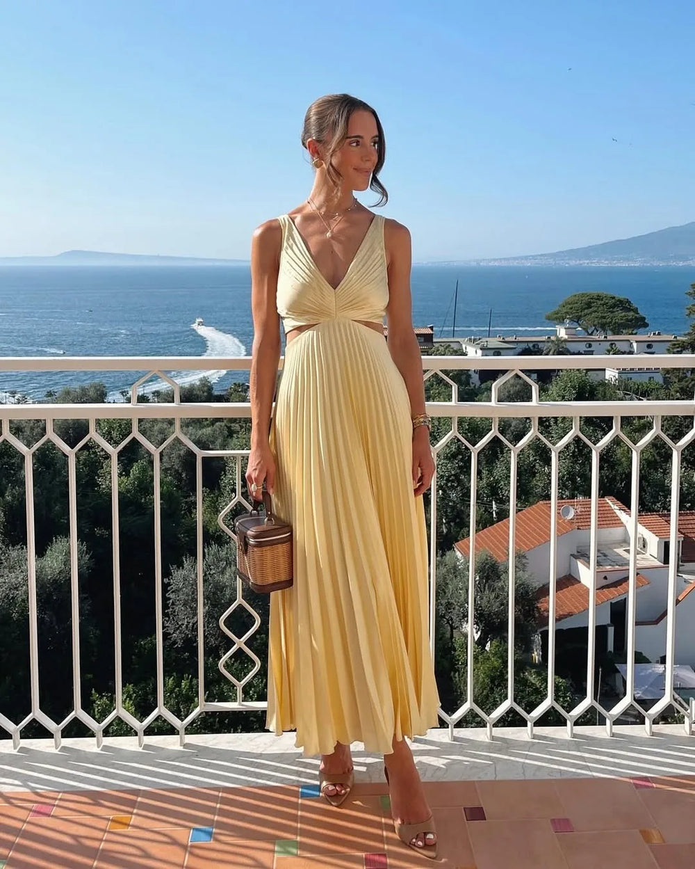 Woman in a yellow pleated cutout midi dress, turned three-quarters to camera