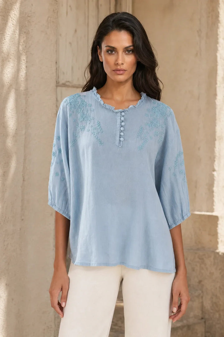 Blue embroidered frill-neck blouse on a model in a contrapposto stance