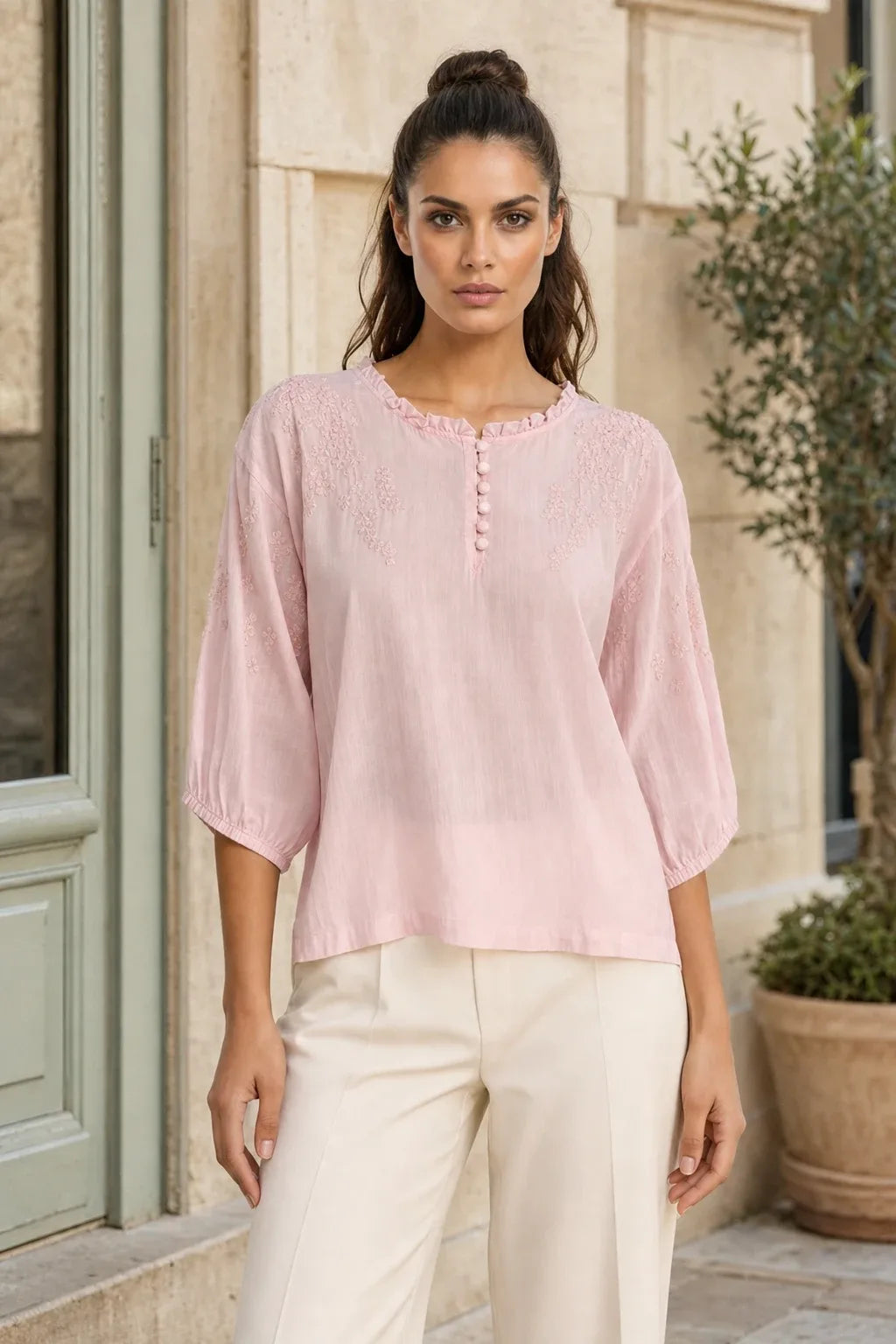 Pink embroidered frill-neck blouse on a model in a contrapposto stance