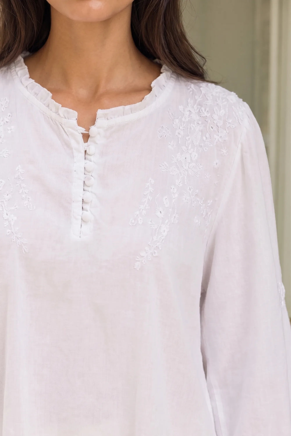 Close-up detail of white blouse showing embroidered frill neckline