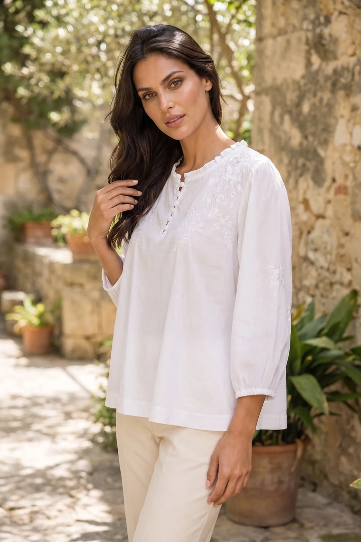 Model wearing a white embroidered frill-neck blouse in a lifestyle setting