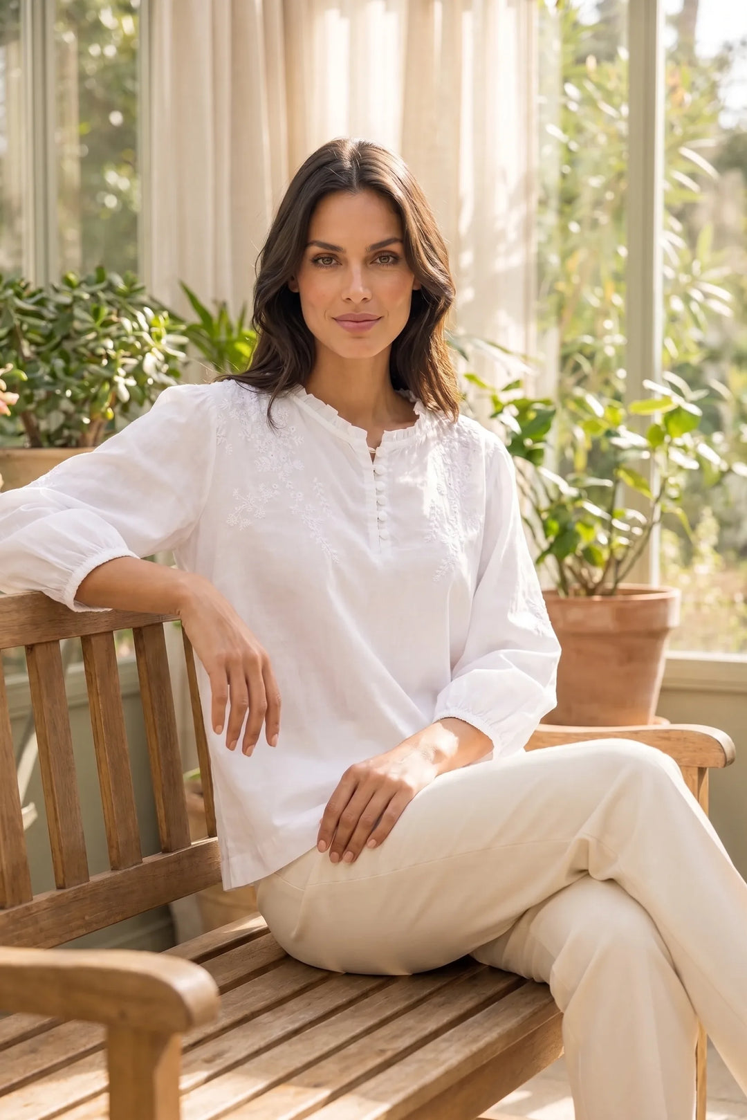 Model wearing a white embroidered frill-neck blouse in an outdoor lifestyle setting