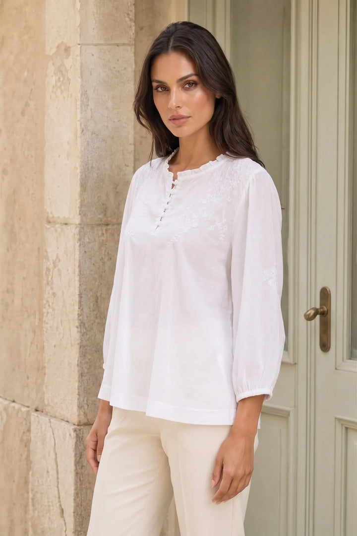 White embroidered frill-neck blouse on a model in a three-quarter turn