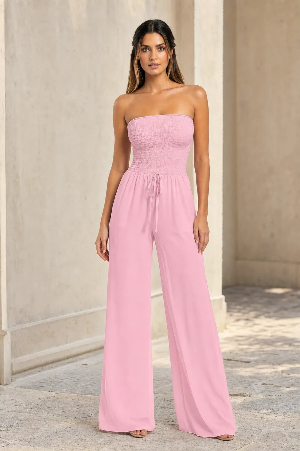 Pink smocked wide leg jumpsuit on model in contrapposto stance, elastic bodice and flowy wide-leg trousers