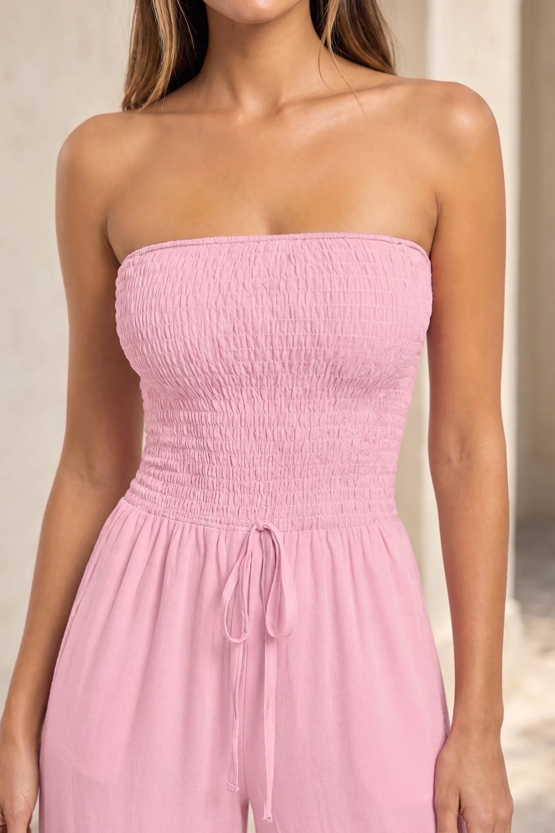 Close-up detail of pink smocked jumpsuit showing elastic smocking texture and fabric