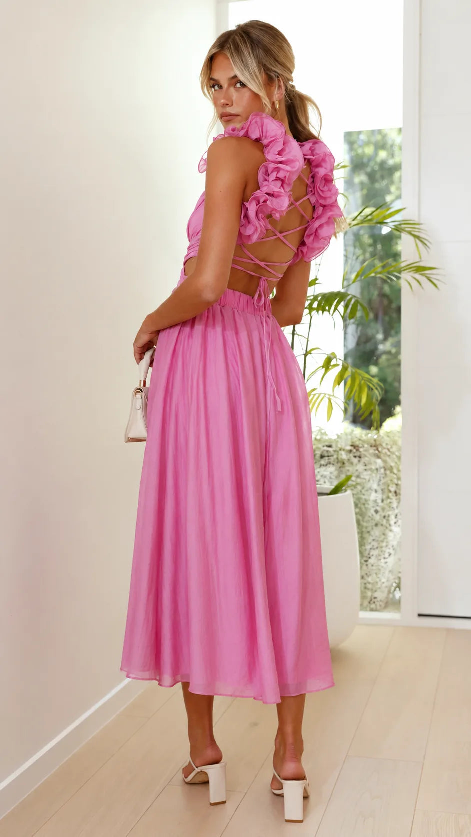Model posing in a pink ruffle midi dress with lace-up bodice detail
