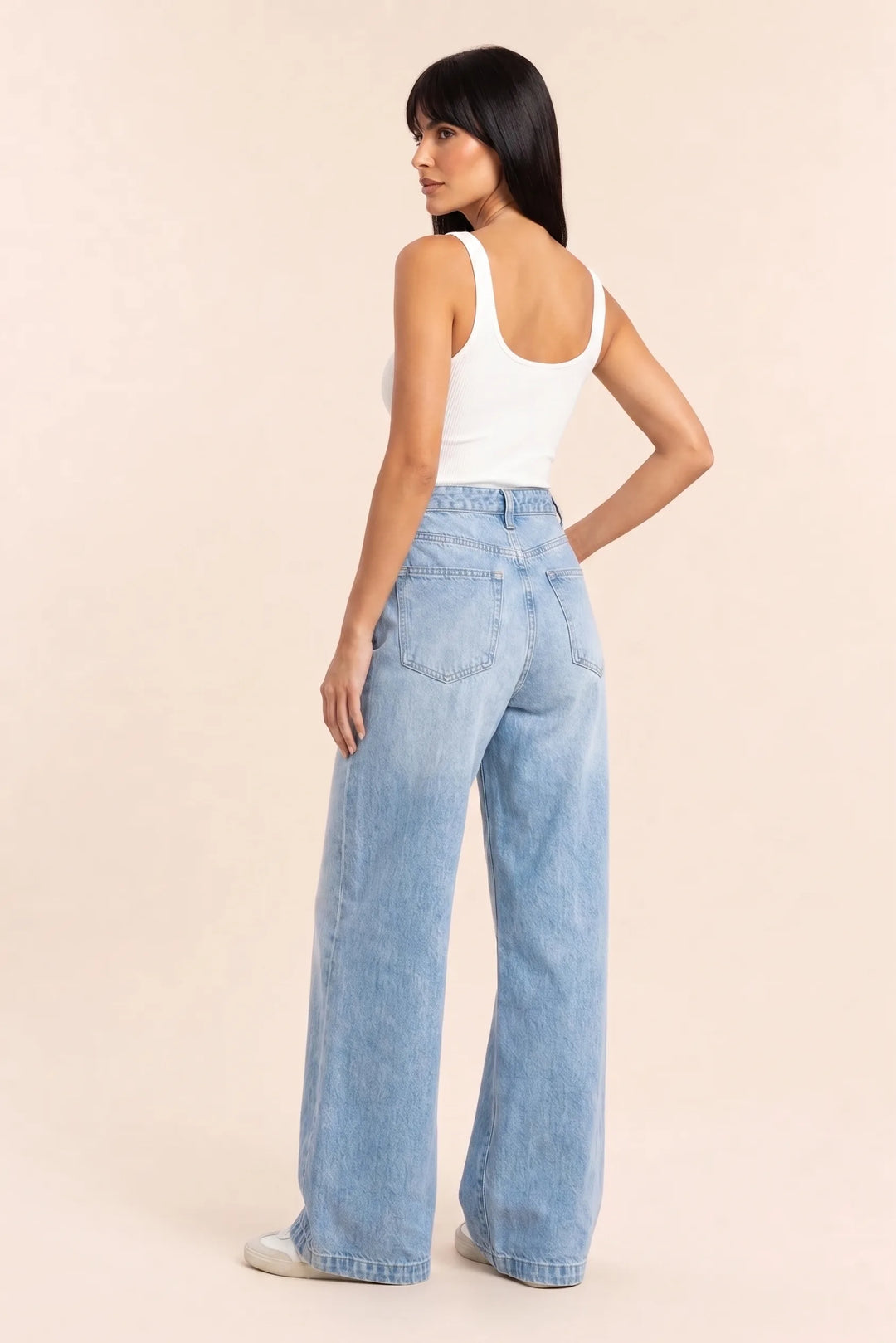 Woman in wide-leg blue jeans and white top, shown from a three-quarter angle
