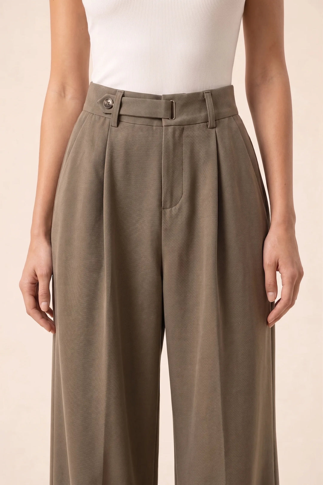 Close-up detail of brown pleated wide-leg trousers showing fabric and pleat construction
