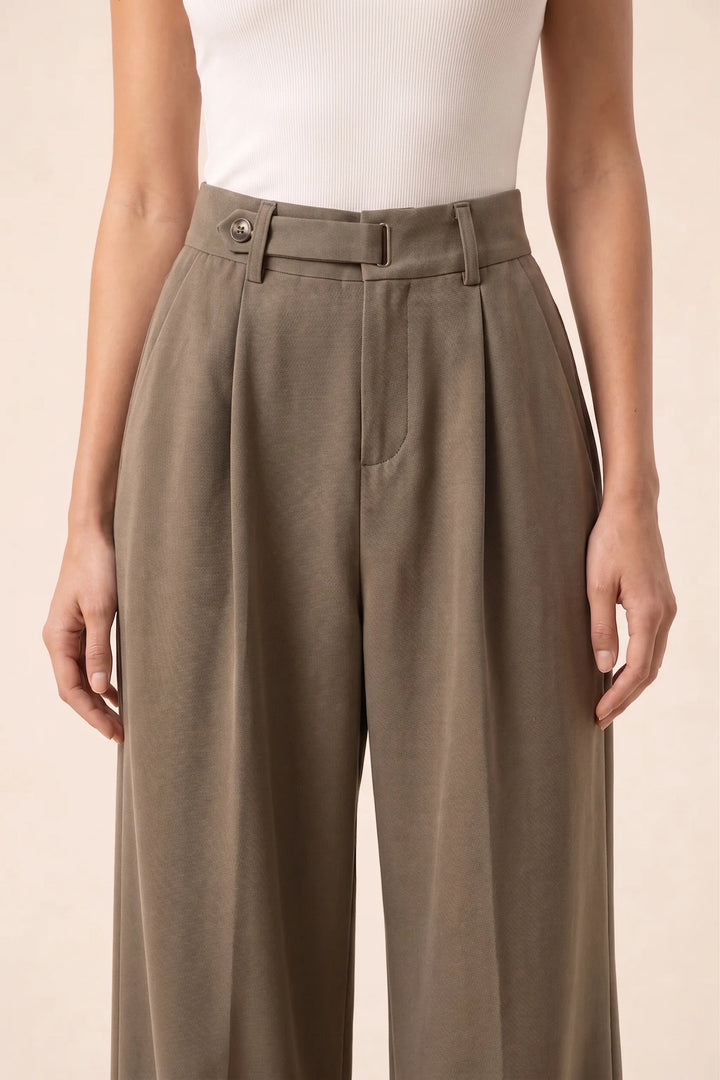 Close-up detail of brown pleated wide-leg trousers showing fabric and pleat construction