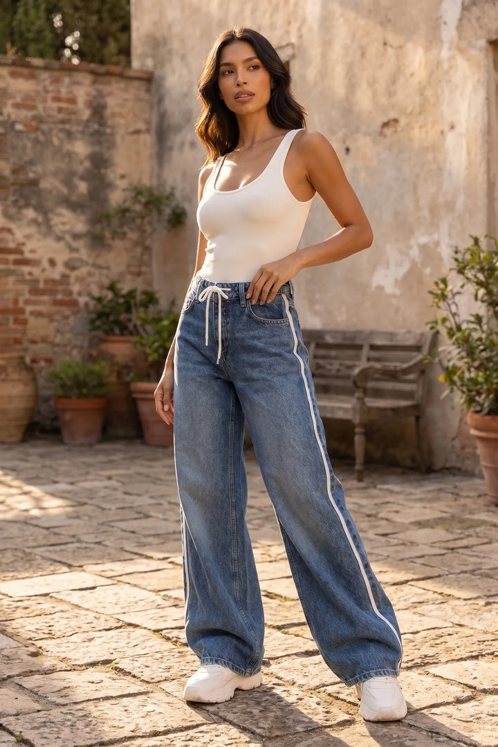 Model wearing medium blue wide-leg jeans with white side stripes in a lifestyle setting