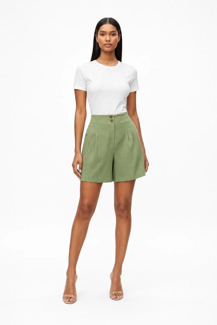 Light green pleated Bermuda shorts on a model in a contrapposto stance