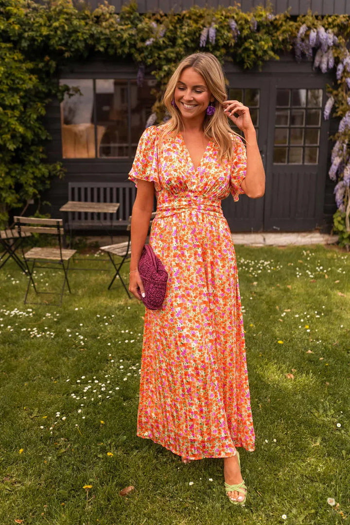 Woman standing facing forward in an orange flutter sleeve maxi dress with flowing tiered skirt