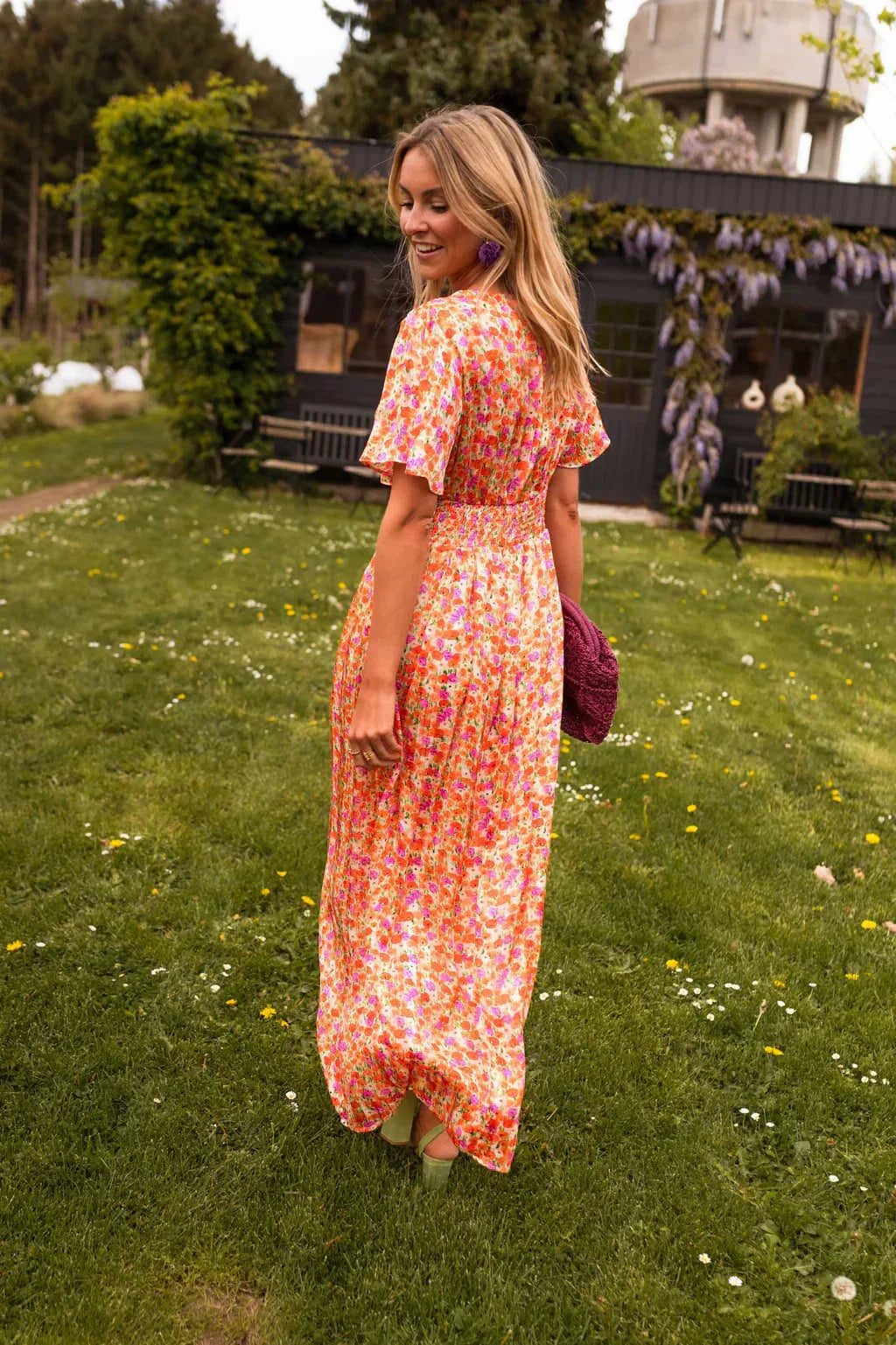 Side view of woman wearing an orange flutter sleeve maxi dress with soft draping details