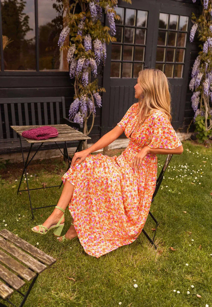 Woman in an orange flutter sleeve maxi dress posed at a three-quarter turn showing silhouette
