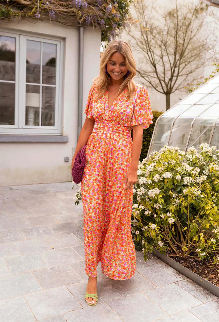 Woman in an orange flutter sleeve maxi dress shown in a styled full-length editorial pose