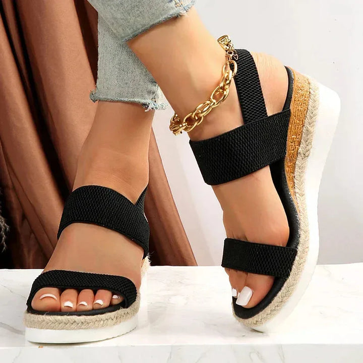 Black wedge espadrille sandal, three-quarter view showing straps and espadrille platform