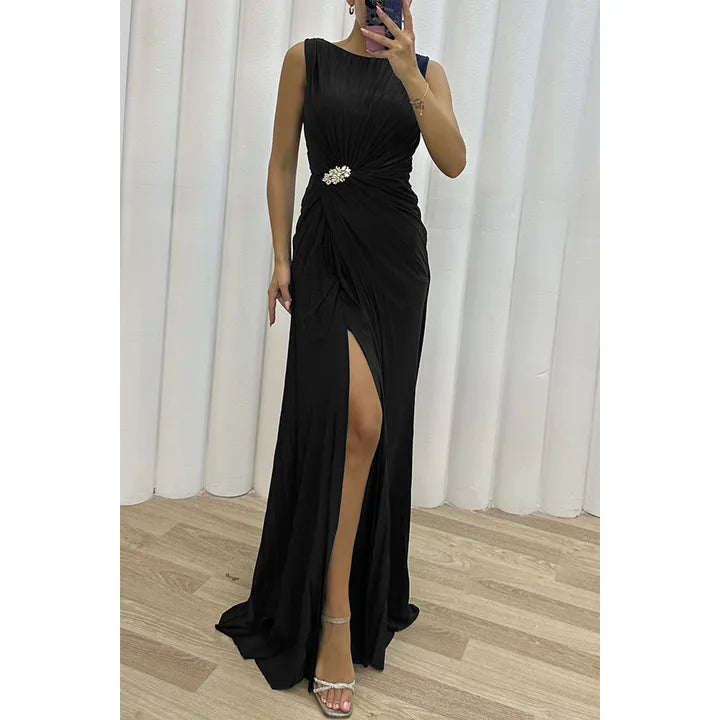 Side view of a woman wearing a black pleated gown with a front slit