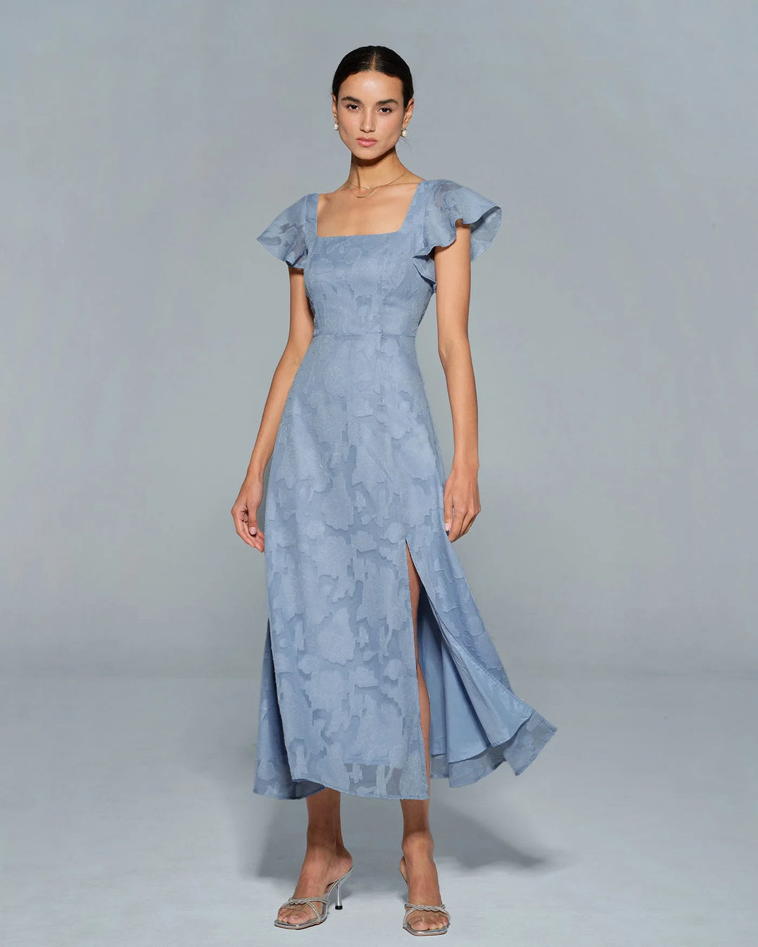 Woman in a blue flutter sleeve midi dress, full-length view from the front