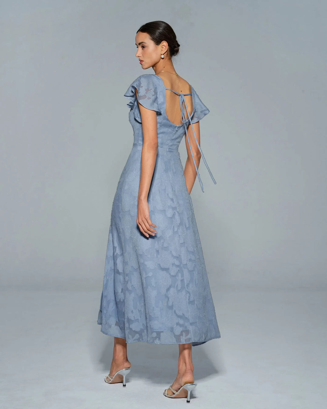 Woman in a blue flutter sleeve midi dress, styled with accessories