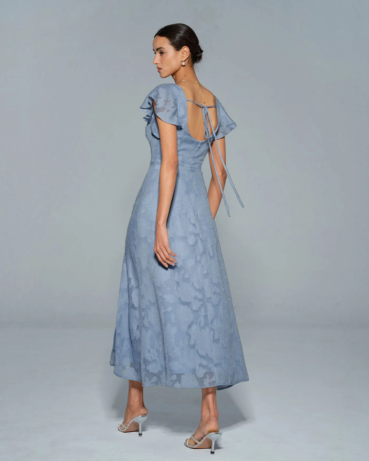 Woman in a blue flutter sleeve midi dress, styled with accessories