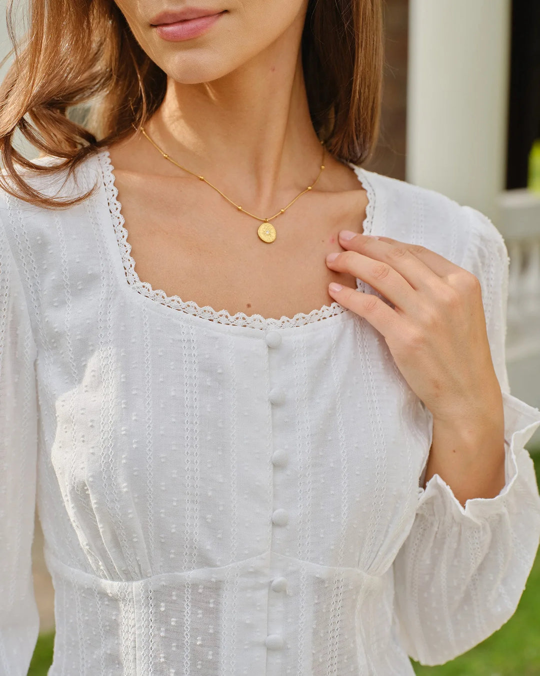Woman in a three-quarter turn showing a white broderie corset blouse with eyelet detail