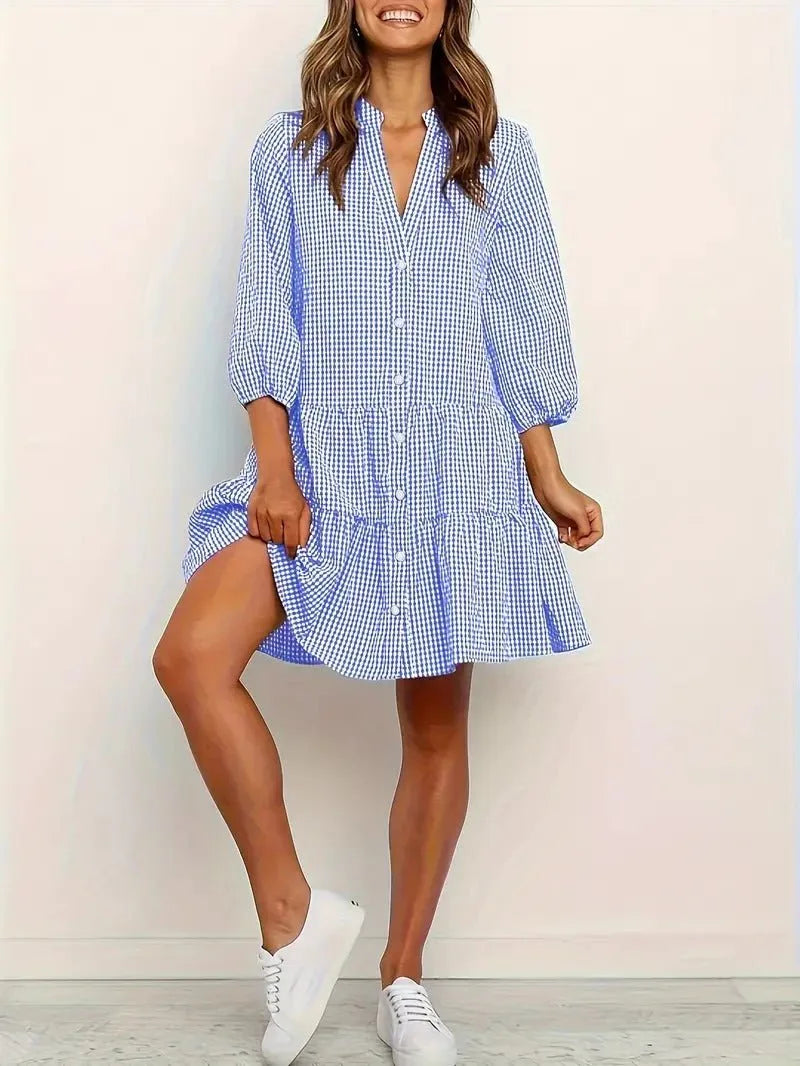 Woman in a blue gingham tiered mini dress shown at a three-quarter turn