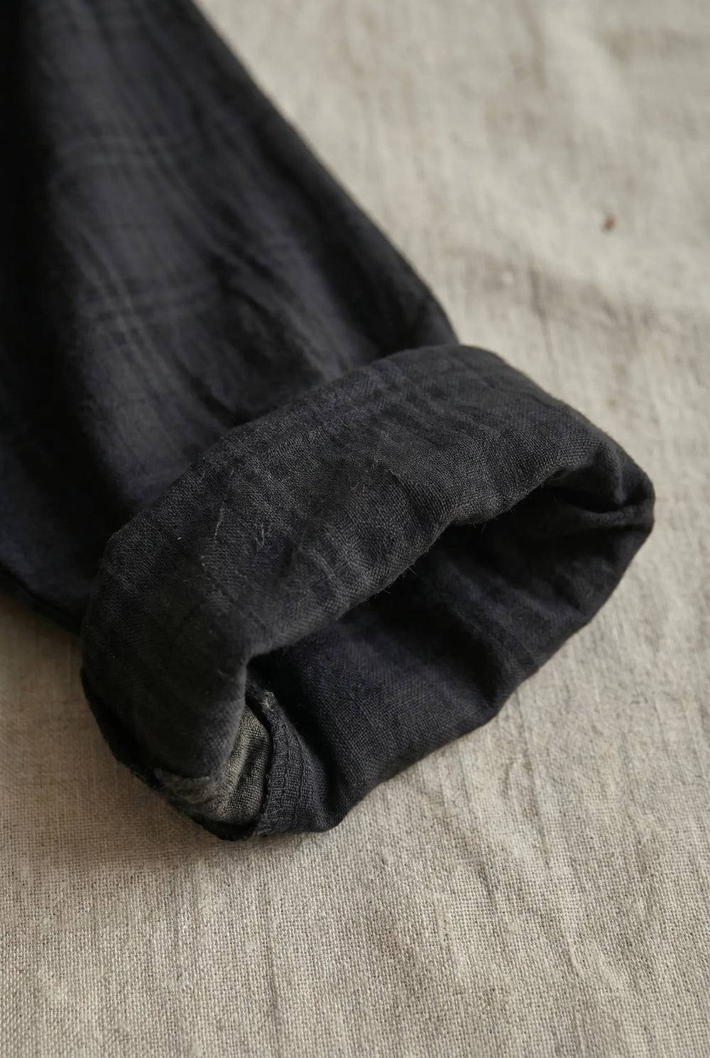 Close-up flatlay detail of black hooded tunic dress highlighting fabric texture and hood construction