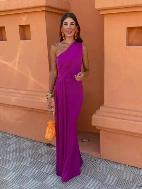 Woman in a three-quarter turn wearing a draped purple one-shoulder maxi dress