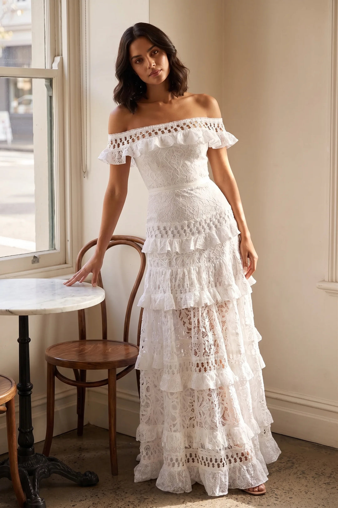 Model wearing white tiered lace gown in lifestyle setting, full-length relaxed pose