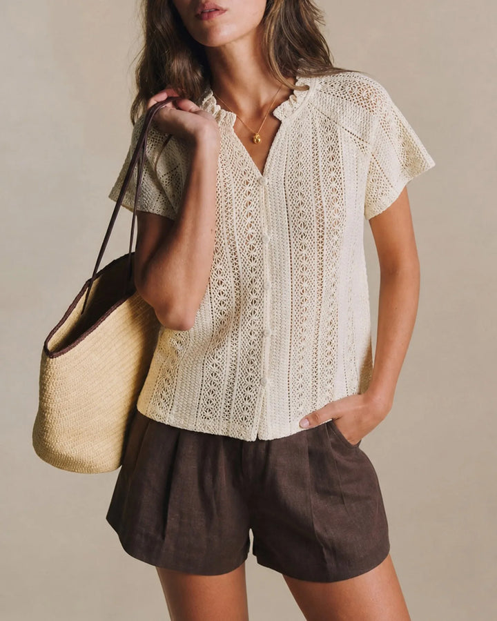 Woman facing forward wearing an apricot crochet blouse with a ruffled neckline
