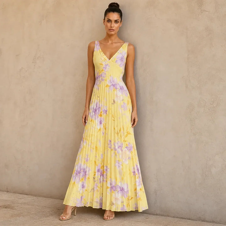 Woman in yellow pleated floral maxi dress standing in contrapposto pose