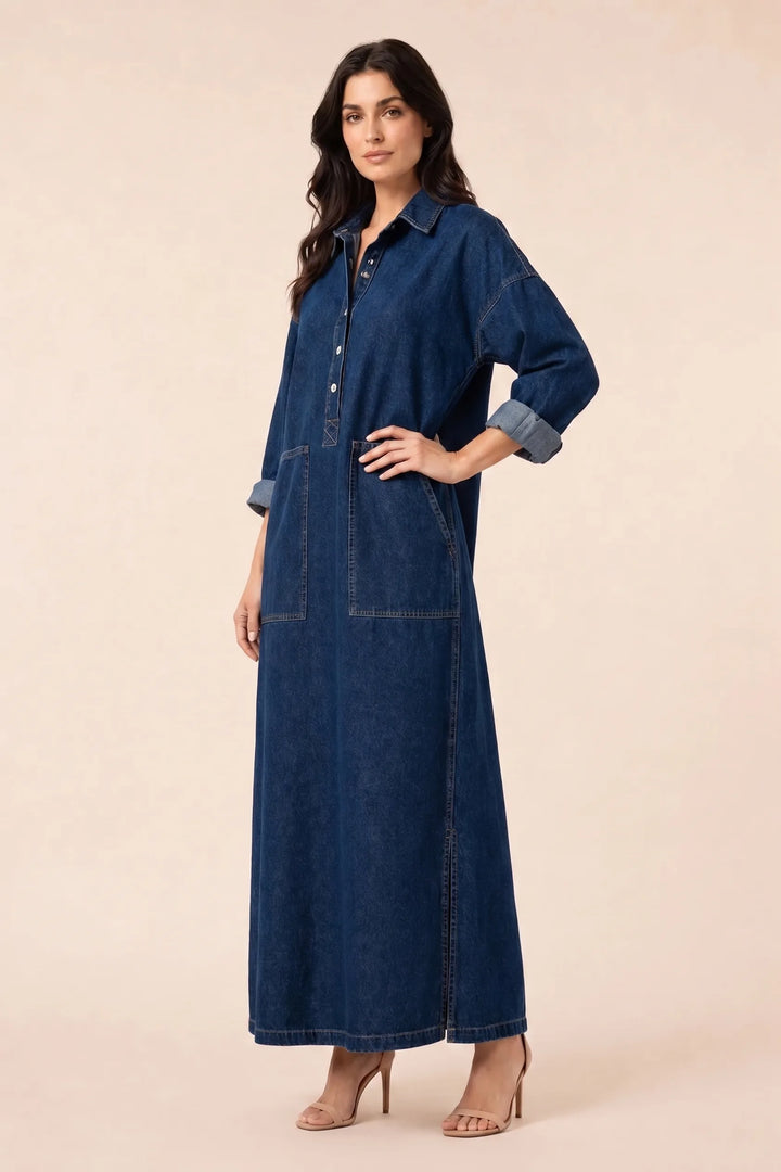 Blue denim maxi dress on model in three-quarter turn, showing back seam and flared hem