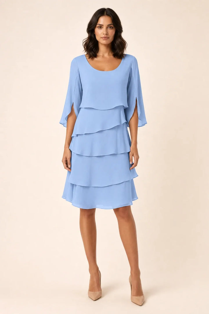 Blue tiered cape dress with flowing layers on a model in a contrapposto stance