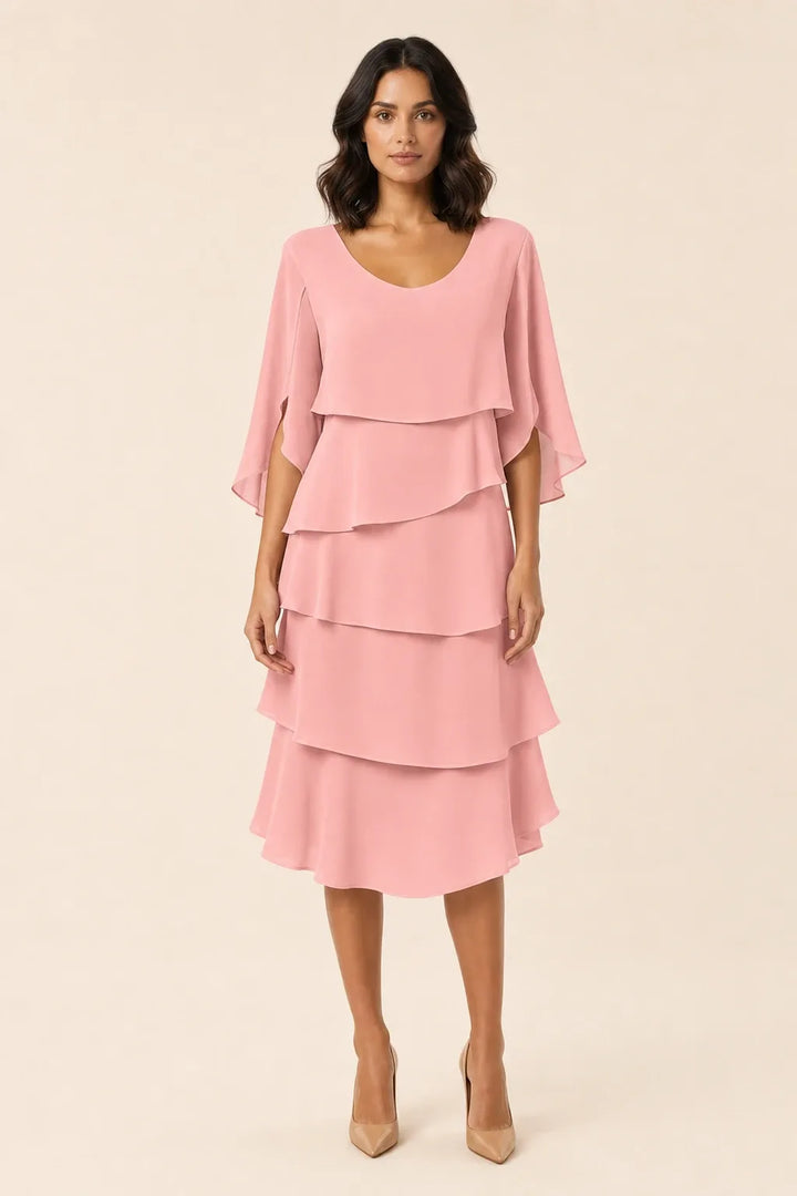Pink tiered cape dress with flowing layers on a model in a contrapposto stance