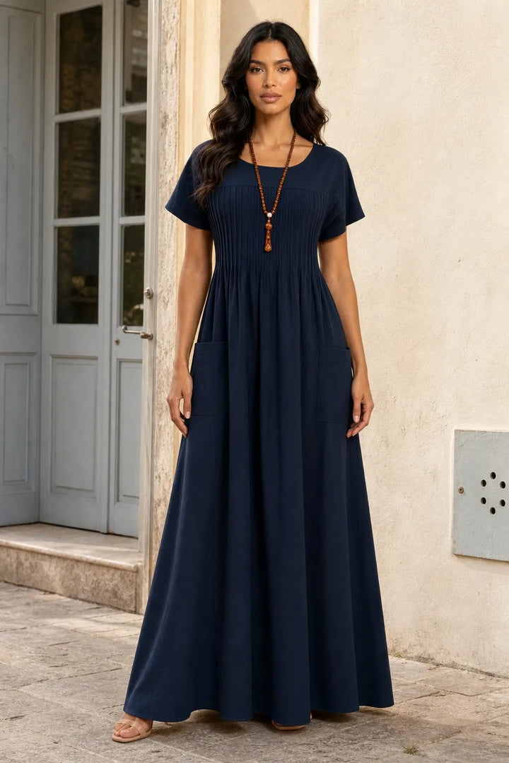 Blue pintuck midi dress on model in contrapposto stance, fitted bodice with vertical pleat detailing