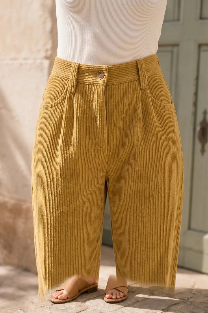 Close-up detail of yellow pleated corduroy pants showing texture and pleats