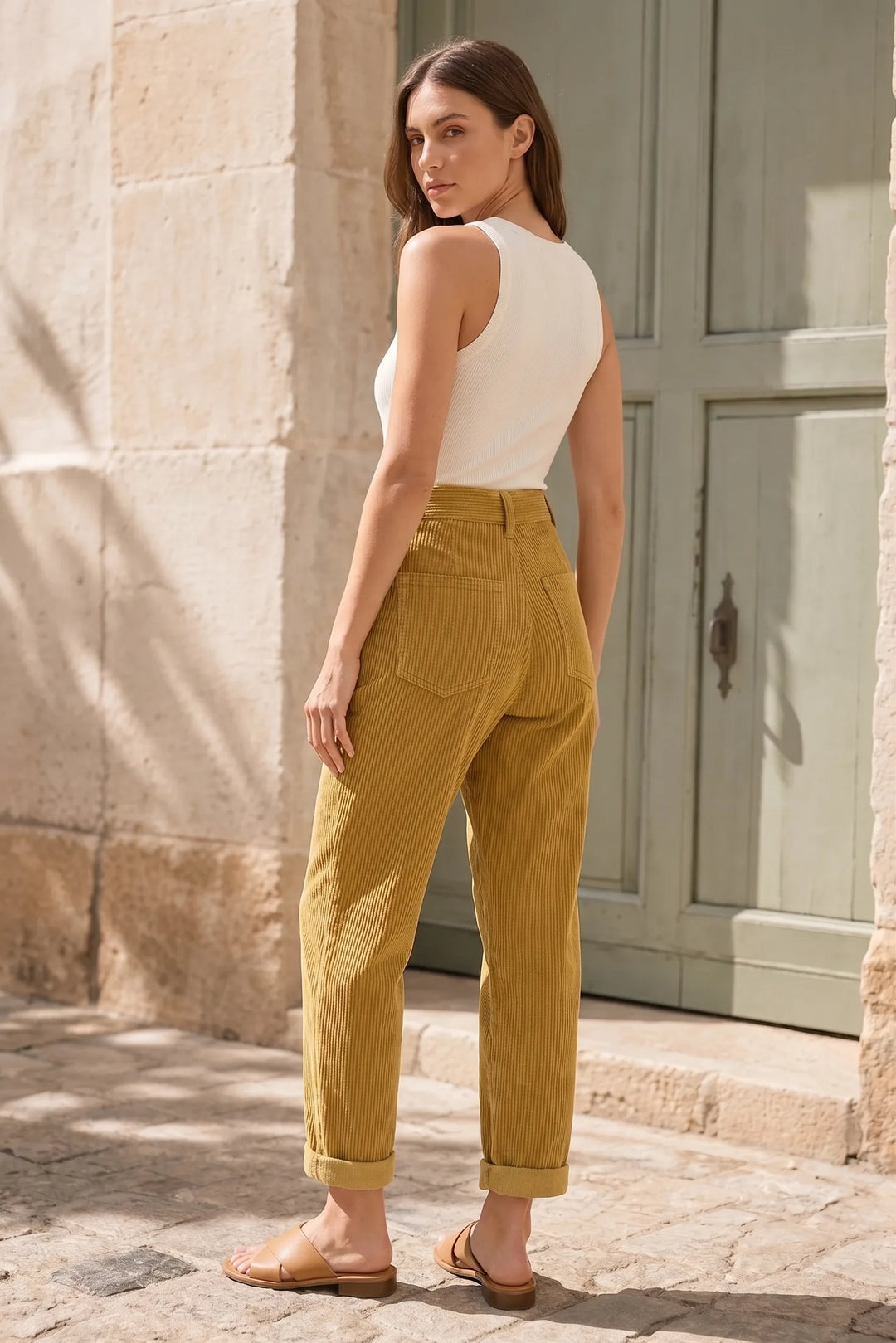 Yellow pleated corduroy pants on a model in a three-quarter turn