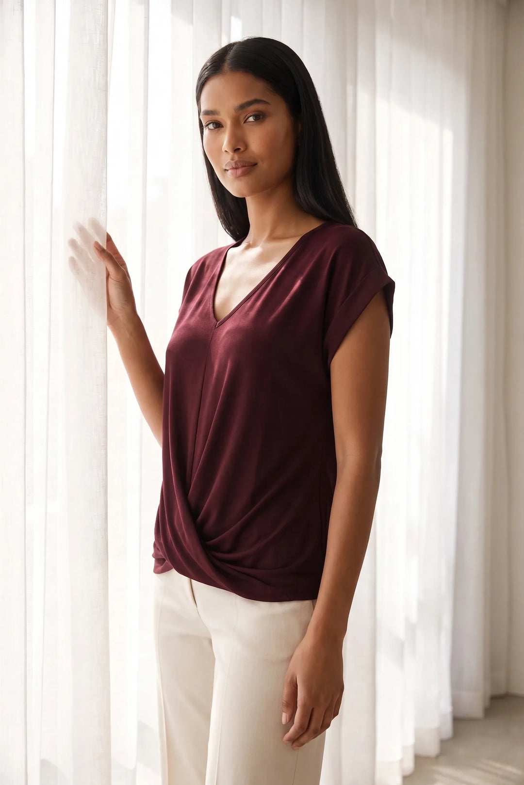 Model wearing a burgundy twist-front cap sleeve top in a lifestyle setting