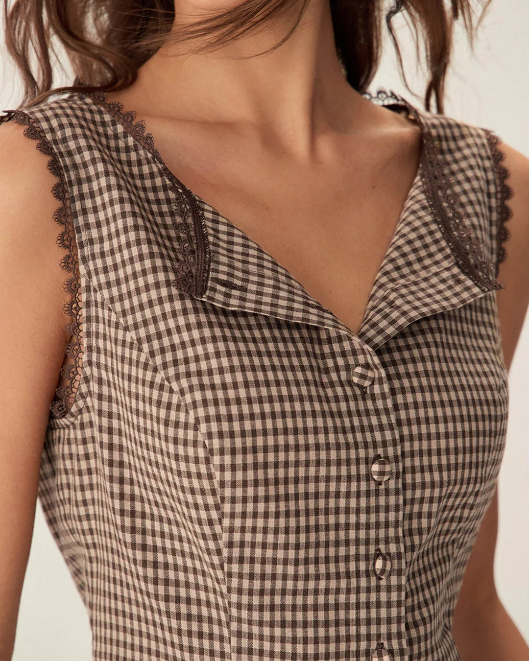Woman in a three-quarter turn wearing a brown gingham top with lace trim