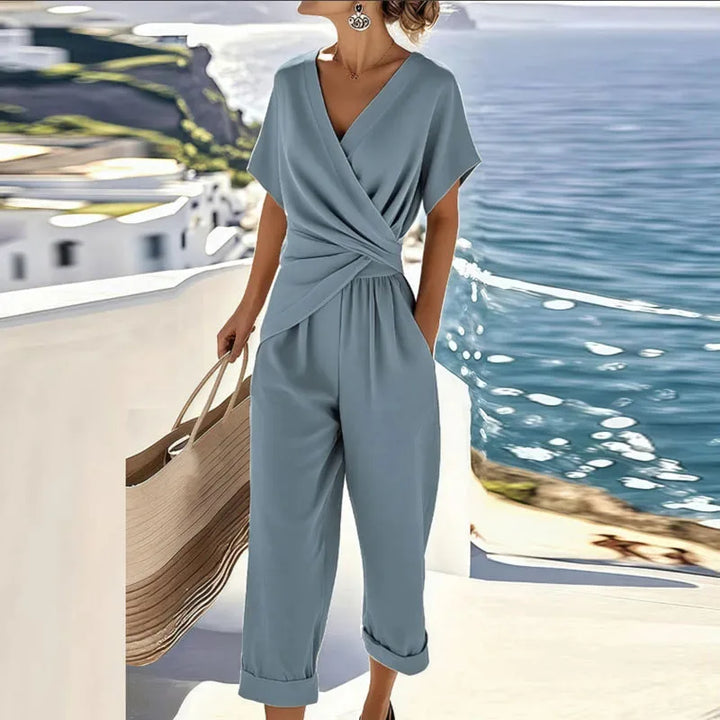 Woman in a blue twisted wrap jumpsuit, turned three-quarters to the camera